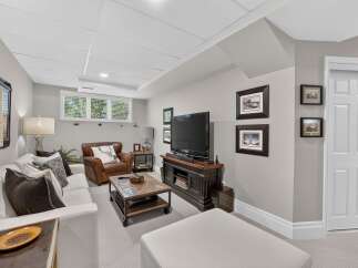 This inviting basement living area features a comfortable white sectional sofa paired with a rich leather armchair, perfect for relaxation.