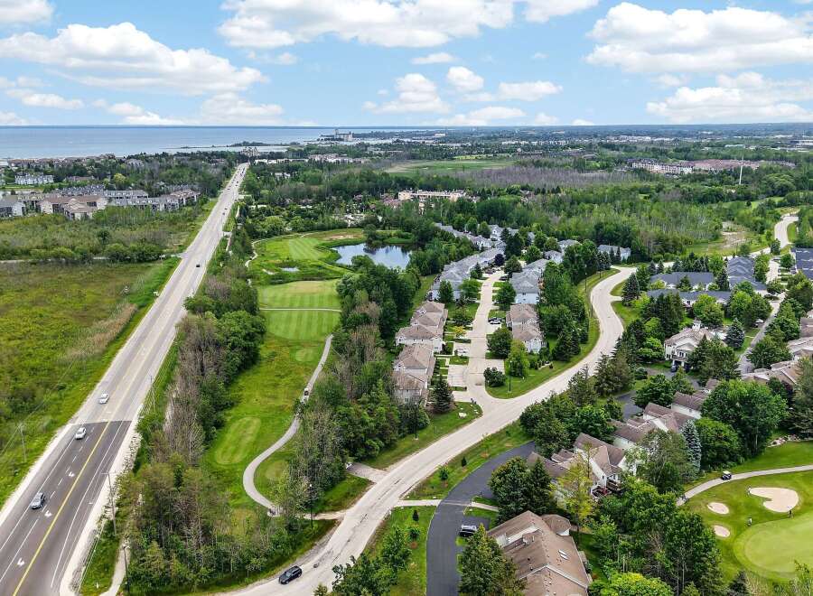 Experience luxury living with this stunning aerial view of a residential community nestled beside a golf course and overlooking a serene body of water.