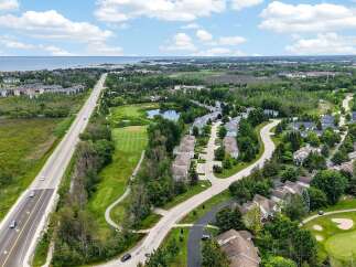 Experience luxury living with this stunning aerial view of a residential community nestled beside a golf course and overlooking a serene body of water.