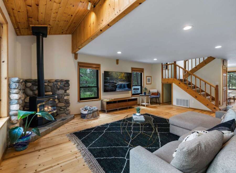 Experience cozy living in this rustic mountain retreat, featuring a stunning stone fireplace and a warm wood-paneled ceiling.
