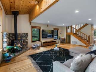 Experience cozy living in this rustic mountain retreat, featuring a stunning stone fireplace and a warm wood-paneled ceiling.