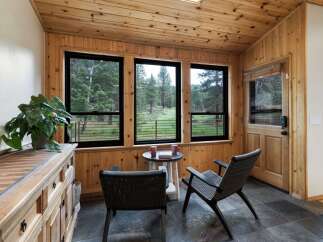 Enjoy the serene forest views from this charming sunroom, featuring abundant natural light and warm wood paneling throughout.