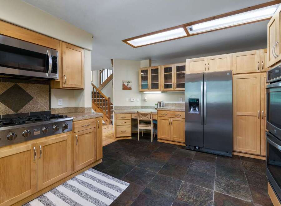 This spacious kitchen features warm wood cabinetry and granite countertops, complemented by stainless steel appliances including a gas range and a double oven.