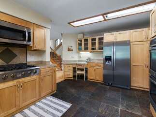 This spacious kitchen features warm wood cabinetry and granite countertops, complemented by stainless steel appliances including a gas range and a double oven.