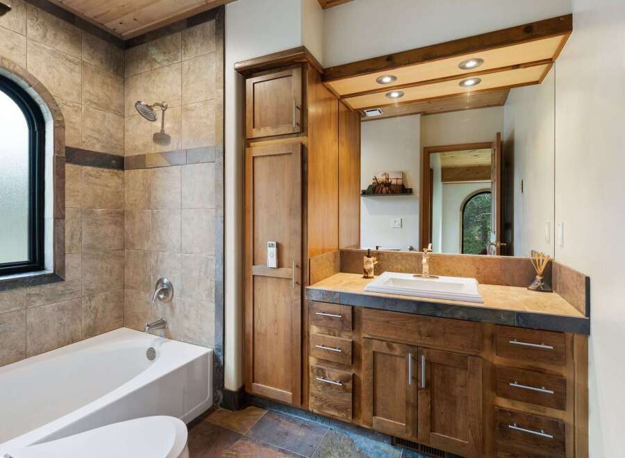 This luxurious bathroom features a spacious bathtub and shower area with elegant tile work and an arched window.