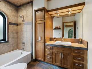 This luxurious bathroom features a spacious bathtub and shower area with elegant tile work and an arched window.