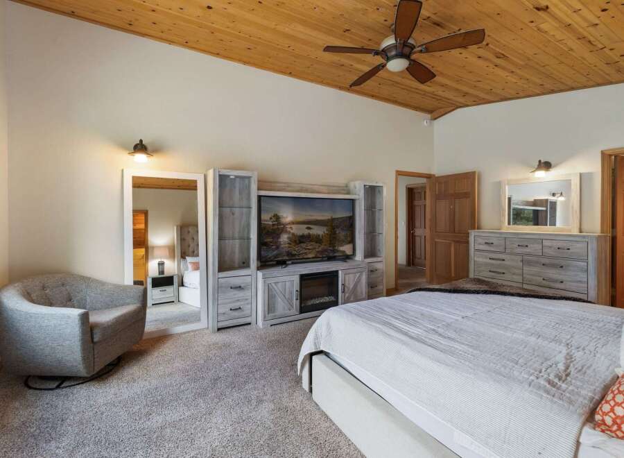 Experience ultimate comfort in this spacious master bedroom, featuring a cozy armchair and a large entertainment center with a fireplace.