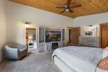 Experience ultimate comfort in this spacious master bedroom, featuring a cozy armchair and a large entertainment center with a fireplace.