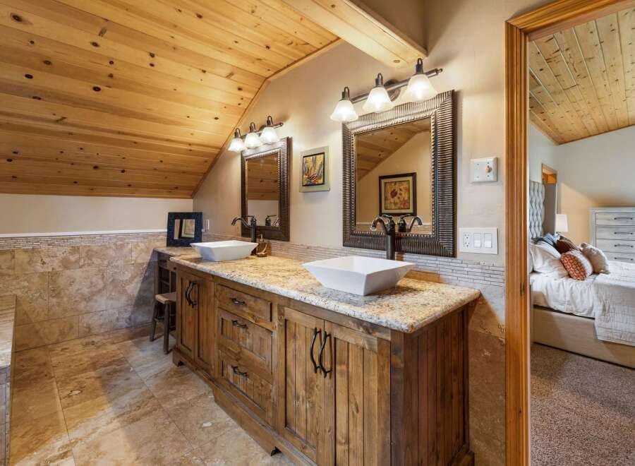 This rustic bathroom features a double vanity with square vessel sinks and granite countertops, complemented by a warm wooden cabinetry and a tiled backsplash.