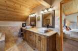 This rustic bathroom features a double vanity with square vessel sinks and granite countertops, complemented by a warm wooden cabinetry and a tiled backsplash.
