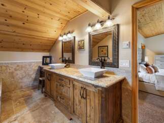 This rustic bathroom features a double vanity with square vessel sinks and granite countertops, complemented by a warm wooden cabinetry and a tiled backsplash.