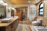 This luxurious bathroom features a spacious double vanity with granite countertops and vessel sinks, complemented by warm wood cabinetry and a wood-paneled ceiling.