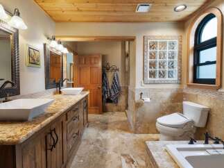 This luxurious bathroom features a spacious double vanity with granite countertops and vessel sinks, complemented by warm wood cabinetry and a wood-paneled ceiling.