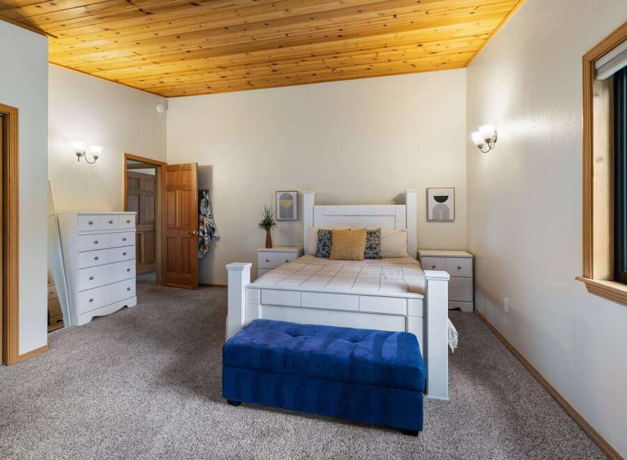 This charming bedroom features a cozy queen-size bed with a white headboard, complemented by a plush blue storage bench at the foot of the bed.