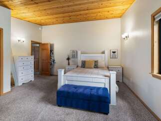 This charming bedroom features a cozy queen-size bed with a white headboard, complemented by a plush blue storage bench at the foot of the bed.