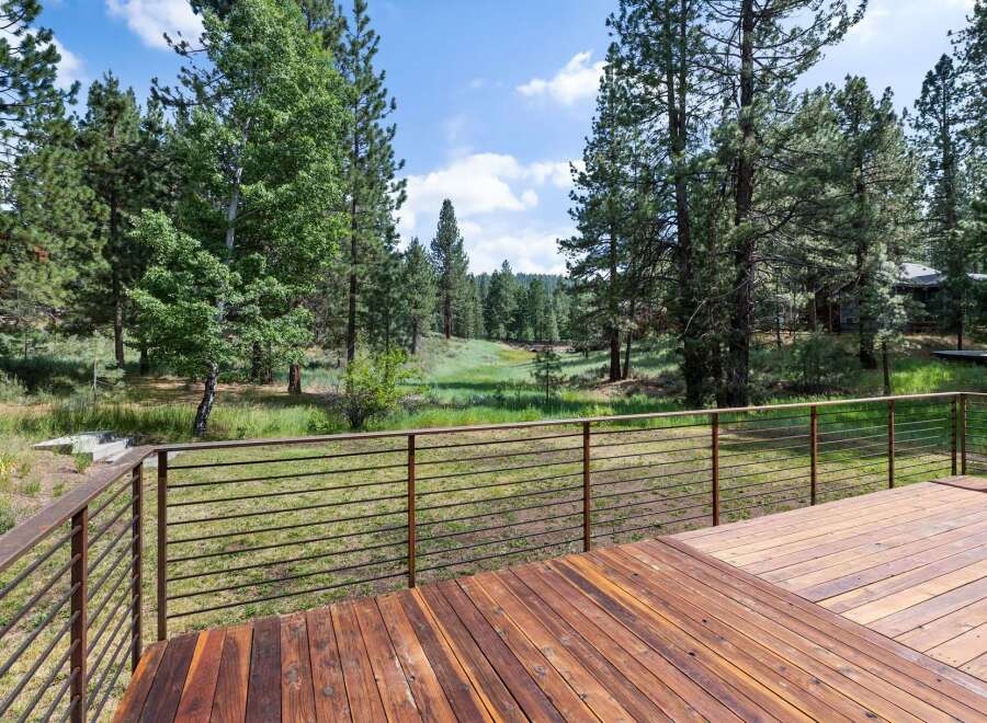 Enjoy the serene natural beauty from this expansive wooden deck, featuring modern metal railings for unobstructed views.