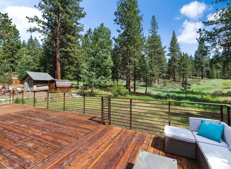 Enjoy the serene mountain lifestyle from this expansive wooden deck, offering breathtaking views of the surrounding pine forest and lush meadow.