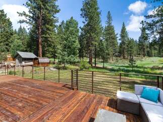 Enjoy the serene mountain lifestyle from this expansive wooden deck, offering breathtaking views of the surrounding pine forest and lush meadow.