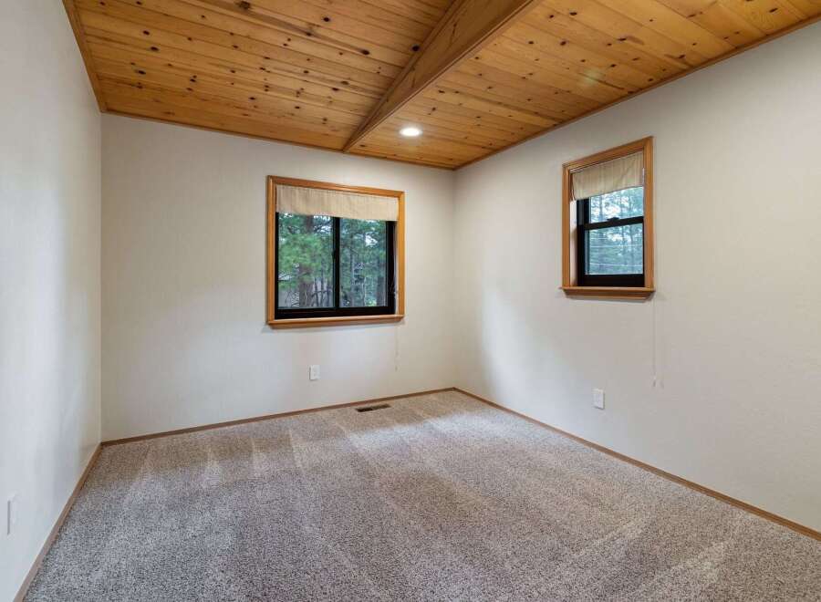 Experience cozy living in this charming room featuring a beautiful wood-paneled vaulted ceiling and large windows that offer scenic views of the surrounding trees.
