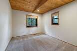 Experience cozy living in this charming room featuring a beautiful wood-paneled vaulted ceiling and large windows that offer scenic views of the surrounding trees.