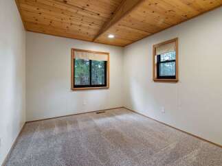 Experience cozy living in this charming room featuring a beautiful wood-paneled vaulted ceiling and large windows that offer scenic views of the surrounding trees.