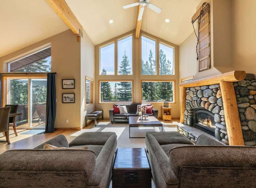 Experience rustic charm and breathtaking views in this stunning living room, featuring a grand stone fireplace and soaring vaulted ceilings with exposed wooden beams.