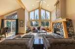 Experience rustic charm and breathtaking views in this stunning living room, featuring a grand stone fireplace and soaring vaulted ceilings with exposed wooden beams.