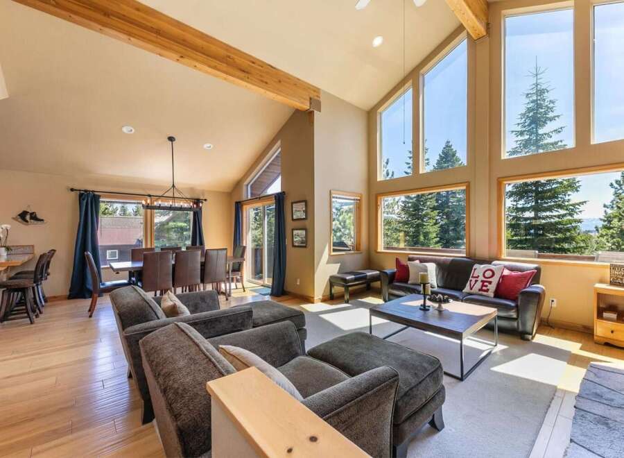 Experience breathtaking mountain views from this stunning living room, featuring a soaring vaulted ceiling with exposed wooden beams and expansive windows that flood the space with natural light.