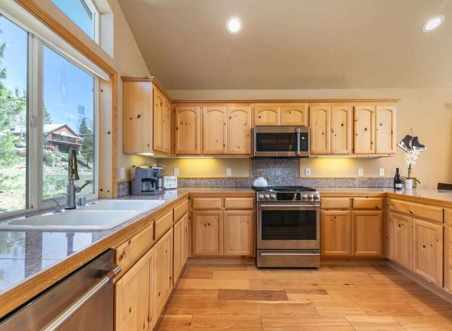 Experience the charm of this rustic kitchen, featuring warm knotty pine cabinetry and a spacious double sink overlooking a picturesque landscape.