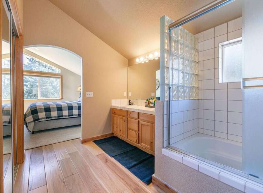 This charming bathroom features a wooden vanity with a tiled countertop and a glass-enclosed shower-tub combo with unique glass block accents.