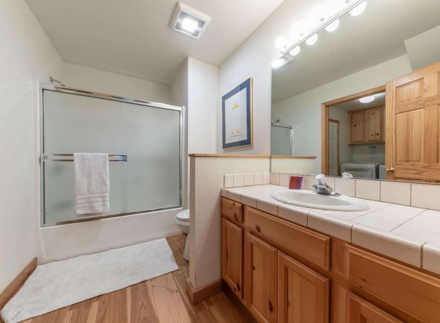 This bright and airy bathroom features a spacious shower with a frosted glass door and a plush white bath mat on the warm wood floor.