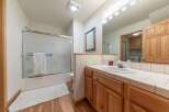 This bright and airy bathroom features a spacious shower with a frosted glass door and a plush white bath mat on the warm wood floor.