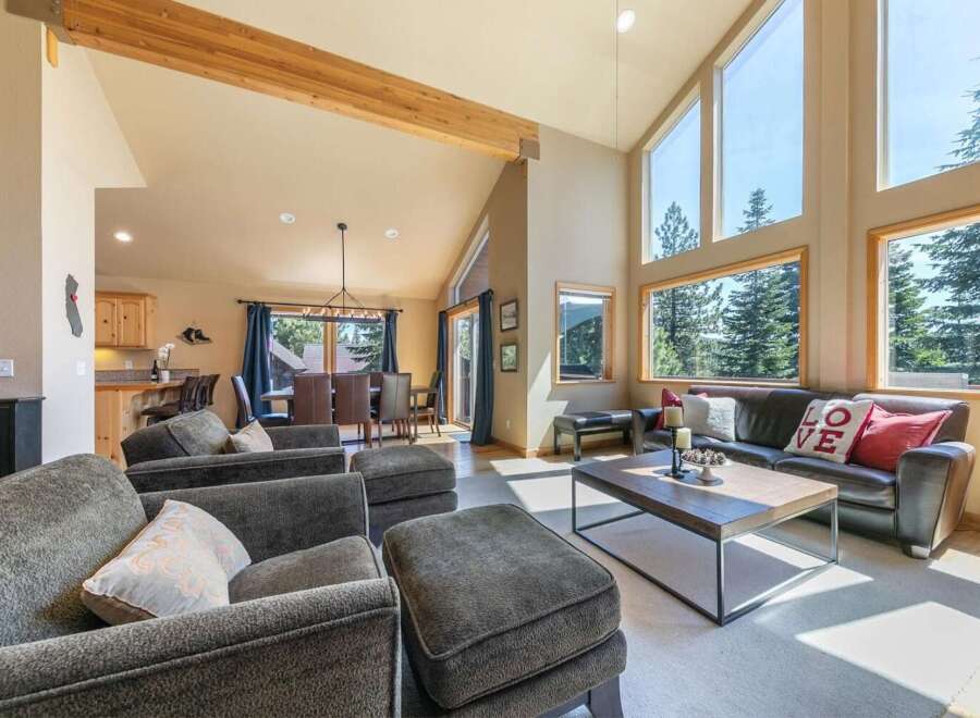 Experience breathtaking mountain views from this stunning living room, featuring a soaring vaulted ceiling with exposed wooden beams and expansive windows that flood the space with natural light.
