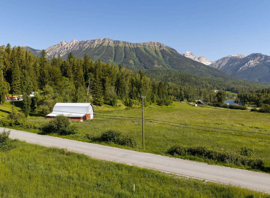 Discover this charming rural property featuring a classic red barn with a silver roof, nestled amidst lush green fields and mature trees.
