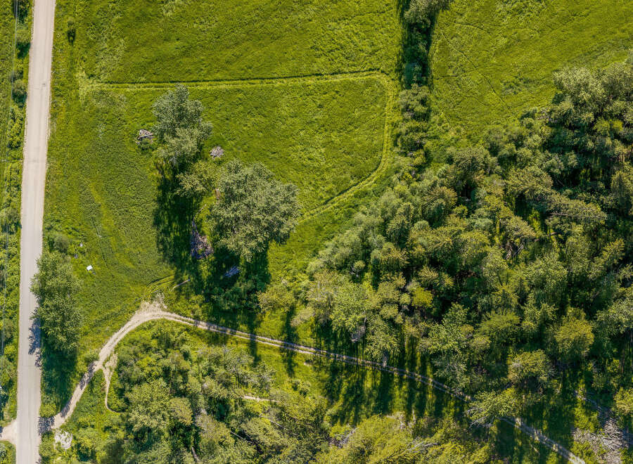 Discover this stunning aerial view showcasing a serene landscape with a paved road winding through lush green fields and dense woodland.