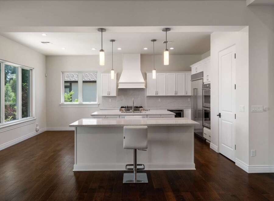 Experience modern luxury in this stunning kitchen, featuring sleek white cabinetry, a spacious island with a waterfall countertop, and a professional-grade range with a striking hood.