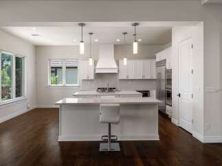 Experience modern luxury in this stunning kitchen, featuring sleek white cabinetry, a spacious island with a waterfall countertop, and a professional-grade range with a striking hood.