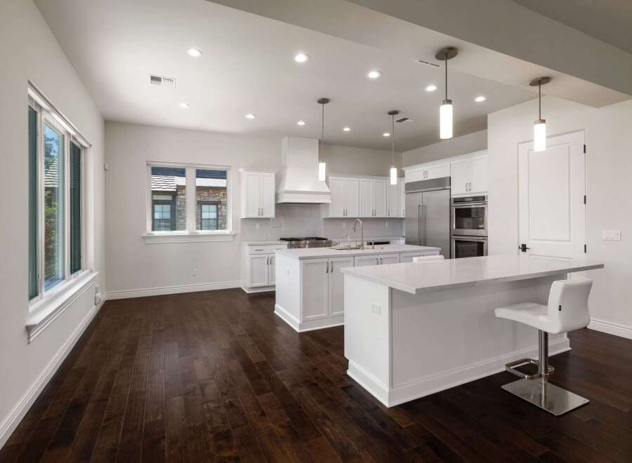 Experience modern luxury in this stunning white kitchen, featuring sleek cabinetry, a spacious island with seating, and top-of-the-line stainless steel appliances.