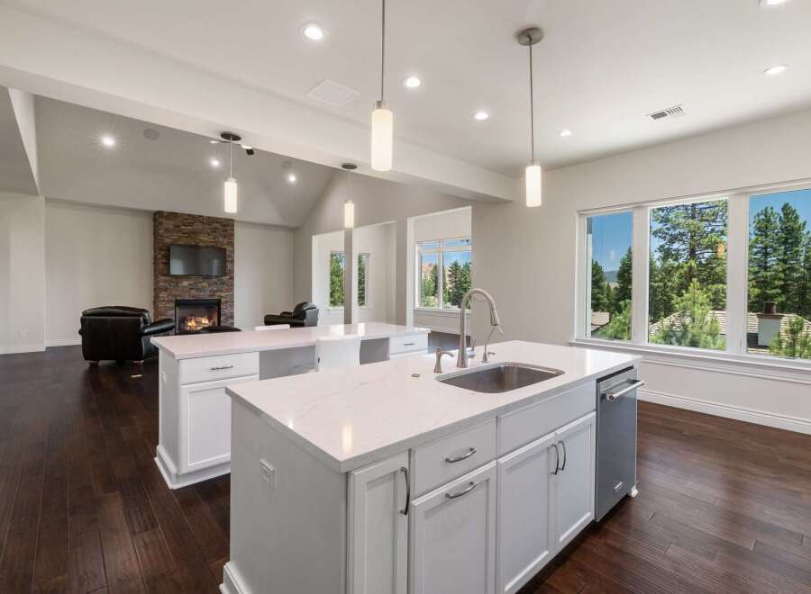 Experience luxury living in this stunning open-concept kitchen and living area, featuring a modern fireplace and expansive windows with breathtaking forest views.