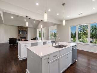 Experience luxury living in this stunning open-concept kitchen and living area, featuring a modern fireplace and expansive windows with breathtaking forest views.