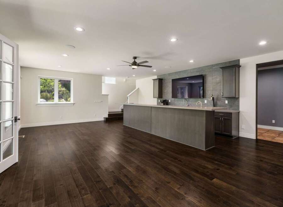 This spacious entertainment area features a modern wet bar with a sleek countertop and ample cabinet space, perfect for hosting guests.