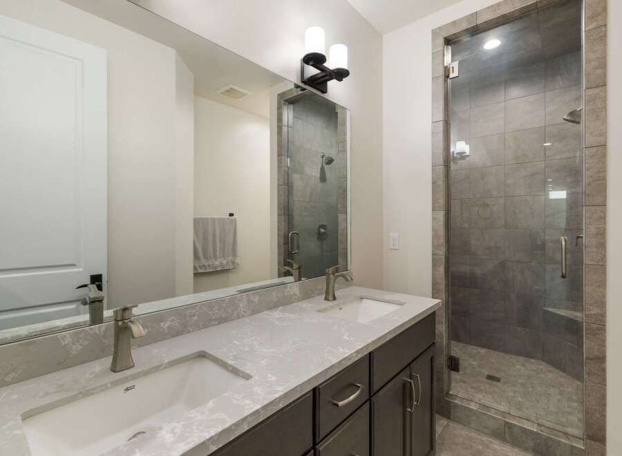 This modern bathroom features a sleek double vanity with a quartz countertop and undermount sinks, complemented by a stylish glass-enclosed shower with stone tile accents.