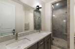 This modern bathroom features a sleek double vanity with a quartz countertop and undermount sinks, complemented by a stylish glass-enclosed shower with stone tile accents.