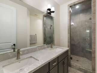 This modern bathroom features a sleek double vanity with a quartz countertop and undermount sinks, complemented by a stylish glass-enclosed shower with stone tile accents.