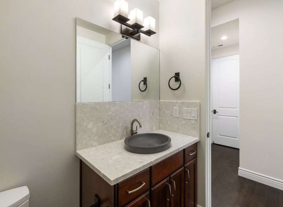 This modern bathroom features a sleek vanity with a dark vessel sink and a speckled quartz countertop.