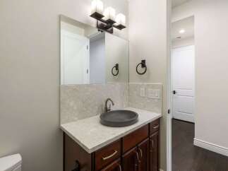 This modern bathroom features a sleek vanity with a dark vessel sink and a speckled quartz countertop.