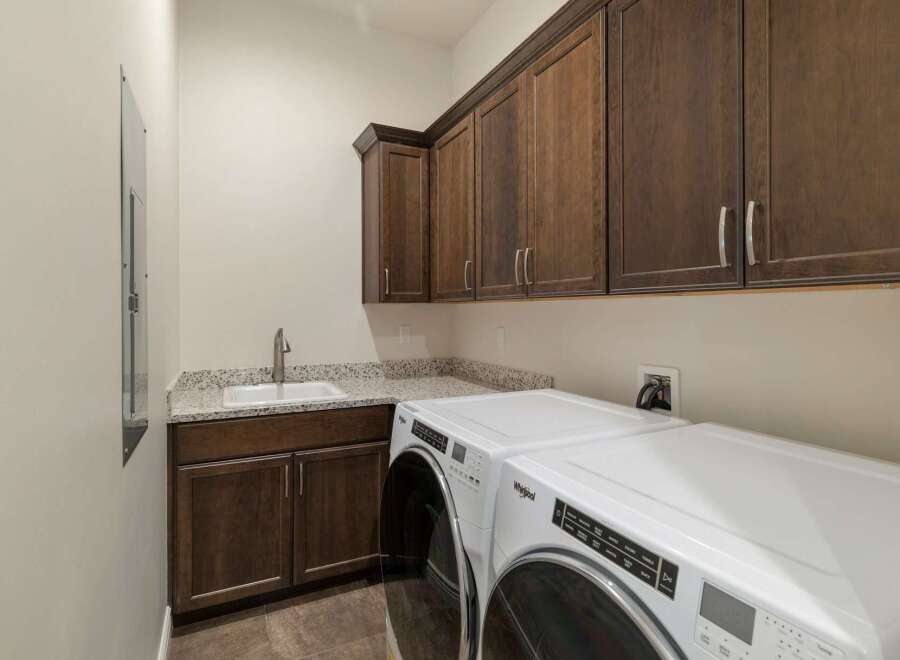 This laundry room boasts ample storage with dark wood cabinetry, both above and below the granite countertop.
