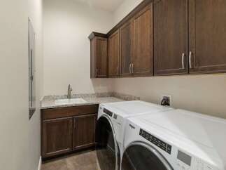 This laundry room boasts ample storage with dark wood cabinetry, both above and below the granite countertop.