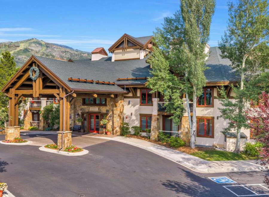 Experience luxury mountain living at this stunning property, featuring a grand entrance with stone accents and a welcoming wooden porte-cochère adorned with a festive wreath.