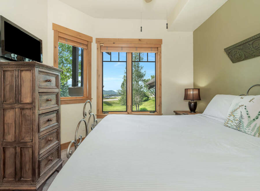 Experience breathtaking mountain views from this charming bedroom, featuring a comfortable king-size bed and a large dresser with a mounted TV.